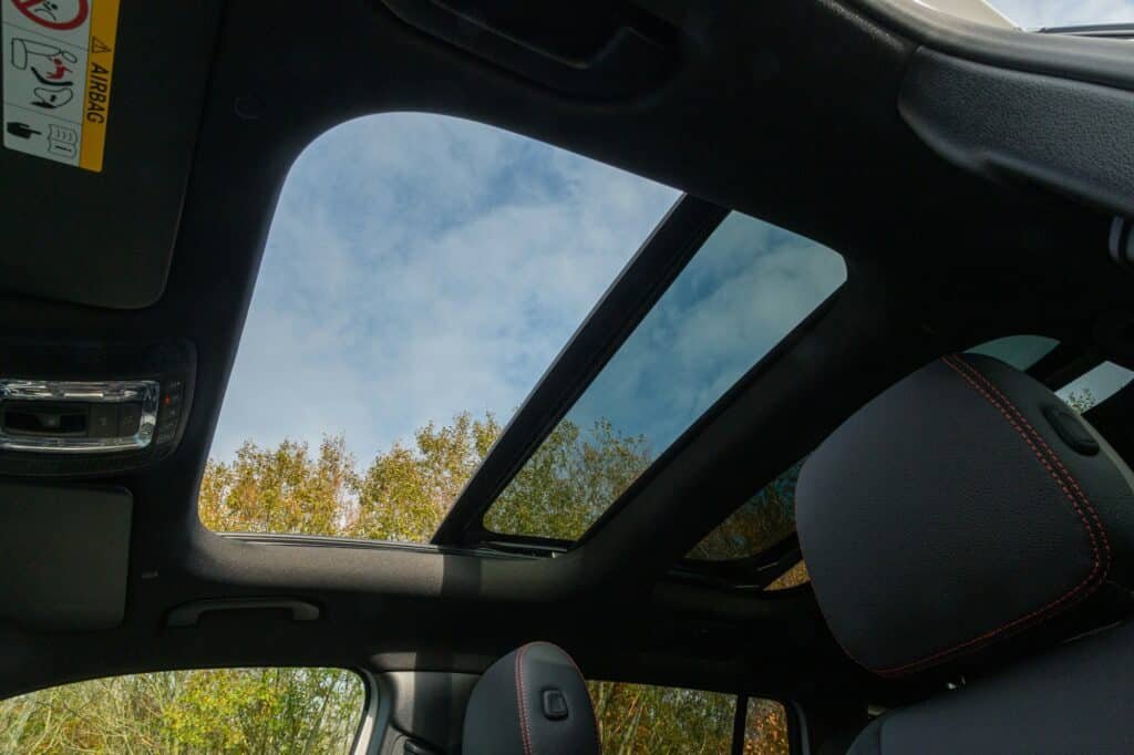 Vue intérieure d'une voiture montrant le toit ouvrant ouvert, laissant entrer la lumière naturelle et offrant une vue du ciel nuageux.